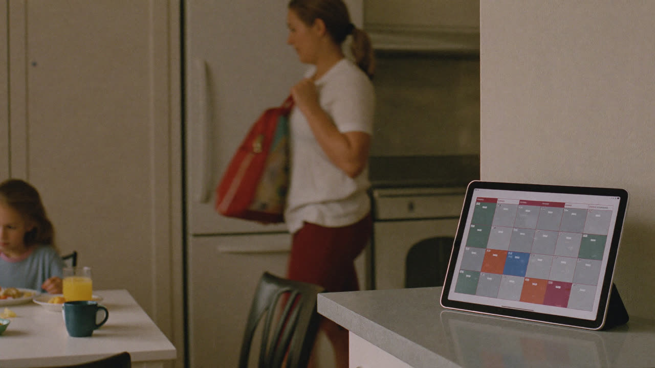 A tablet on the kitchen counter showing the family calendar while the school-morning happens around it.